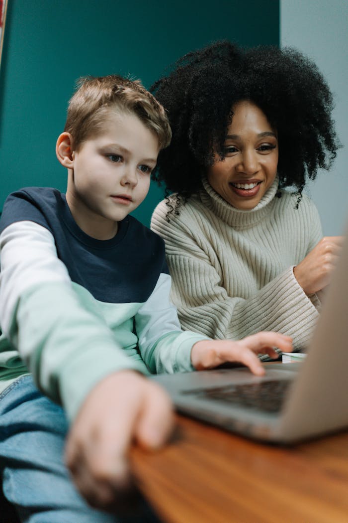 A woman guides a child using a laptop, showcasing diverse learning in a cozy setting.