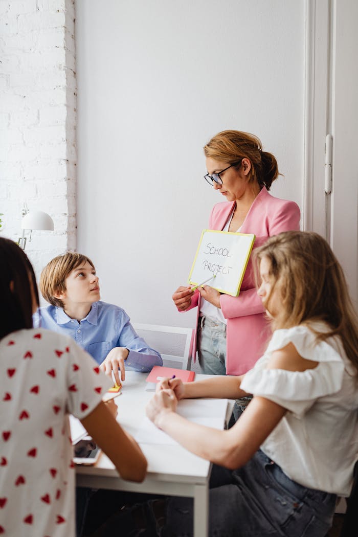 A teacher engages with students during a school project discussion using a whiteboard in a classroom.