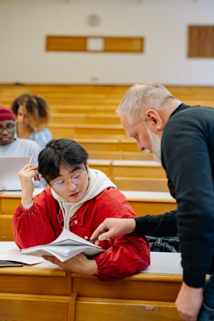 A teacher helps a student with coursework in a university lecture hall setting.
